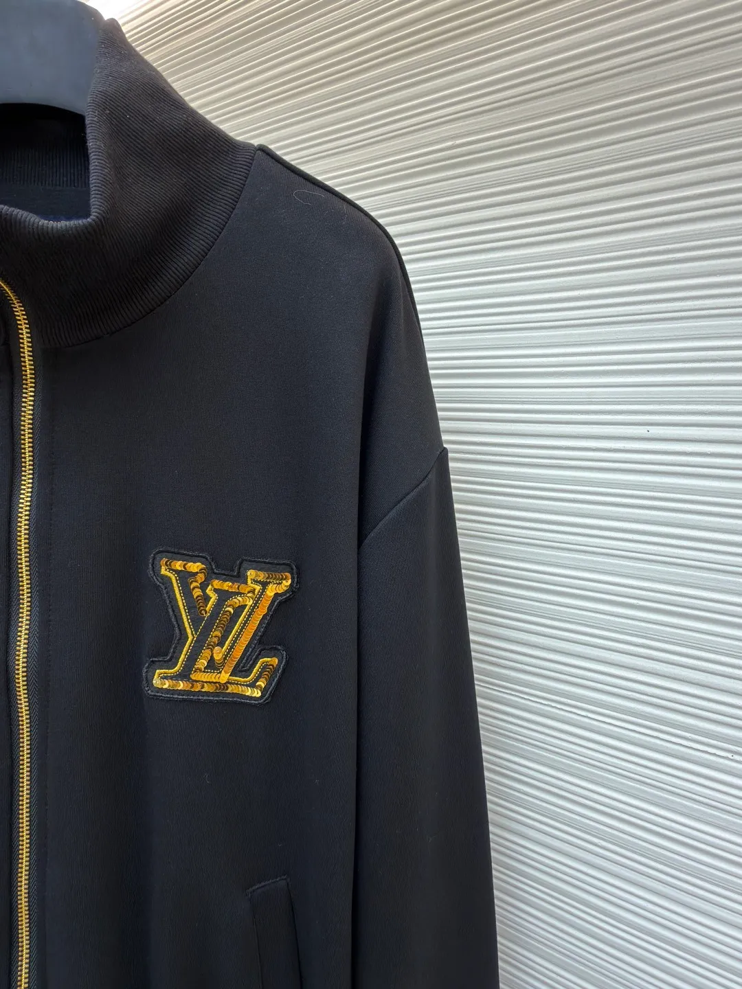LOUIS VUITTON stand-up collar ribbed hem long-sleeved logo decorated jacket ●Original version: Purchased and developed at 25899 ●Item number: 1682404-B25 ●Fabric: cotton fabric ●Technology: knitted production ●Color: black ●Version: fitted version ●Weight: about 990 grams ●Size: S-M-L-XL ●Description: This Louis Vuitton stand-collar zipper jacket is made of high-thread-count cotton-elastic blended fabric, which has been treated with enzyme washing process. The fabric is soft to the touch and has good wrinkle resistance and elasticity. The body has a delicate matte texture. The LV logo on the chest uses a combination of gold thread embroidery and patchwork. The embroidery uses interlaced flat stitch and chain stitch techniques. The stitch density reaches 12 stitches per centimeter. The edges are overlocked and the pattern is three-dimensional and not easy to fall off. The jacket adopts a stand-up collar design, and the collar ribs are made of spandex blended material, which has been shaped to ensure that it will not loosen after long-term wear. The front is equipped with a custom brass zipper, and the zipper teeth are polished and gold-plated, making it smooth, wear-resistant and of high-quality texture. The side seam pockets are welted, and the seams are reinforced with double-needle sewing. The ribbed edges of the cuffs and hem are woven with high-elastic yarns of the same color. The shoulders are seamlessly spliced ​​with natural shoulder shapes. The overall craftsmanship combines the brand's classic elements with practical design, fully demonstrating the production level of high-end clothing. The overall wiring is straight and delicate, the fabric is comfortable and soft, and the color is consistent without color difference. It can be matched with the same style to create a fashionable look and control various occasions. Customized accessories, complete with three standards, same style for men and women!